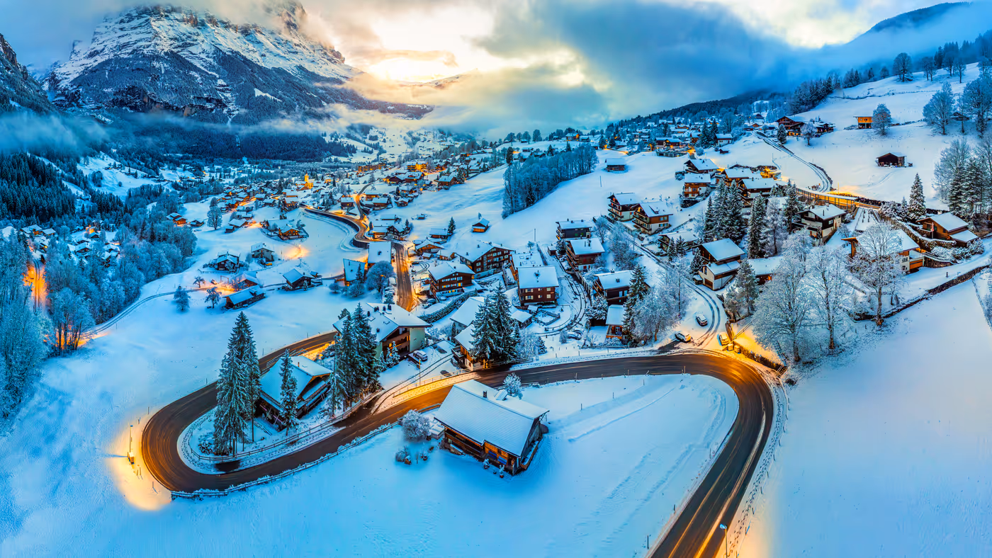 Snow-covered Alpine village and winding mountain road at dusk